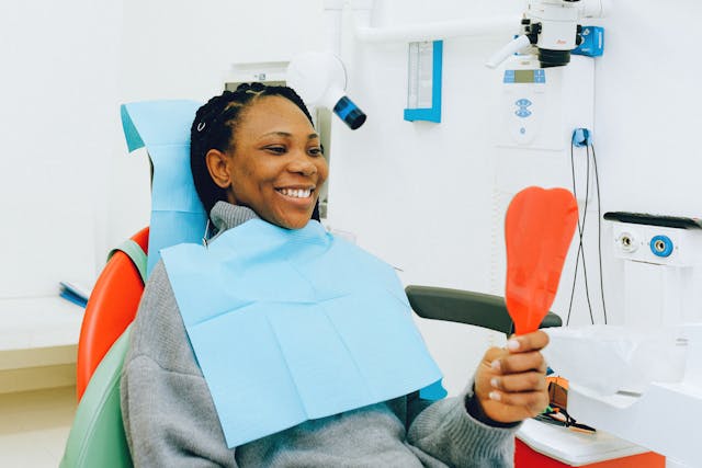 General Dentistry DentMind Nairobi CBD - lady in chair smiling holding a mirror to her teeth after a Dental checkup