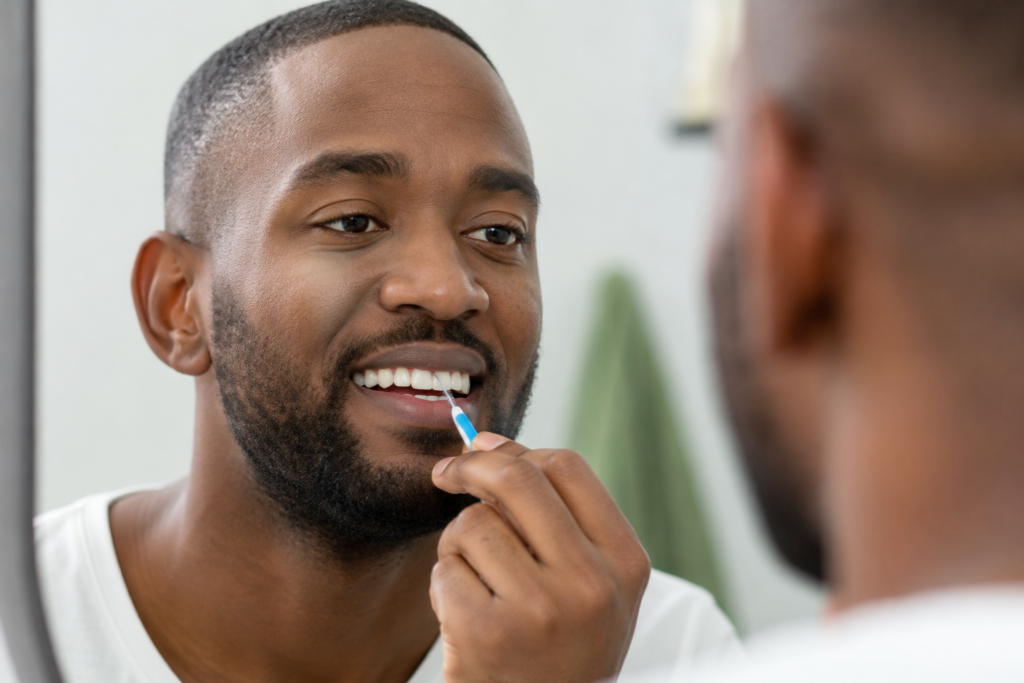 Person cleaning between teeth with an interdental brush for dental implants aftercare.