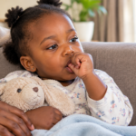 Toddler sucking thumb on a sofa, showing thumb sucking teeth habit in young children.